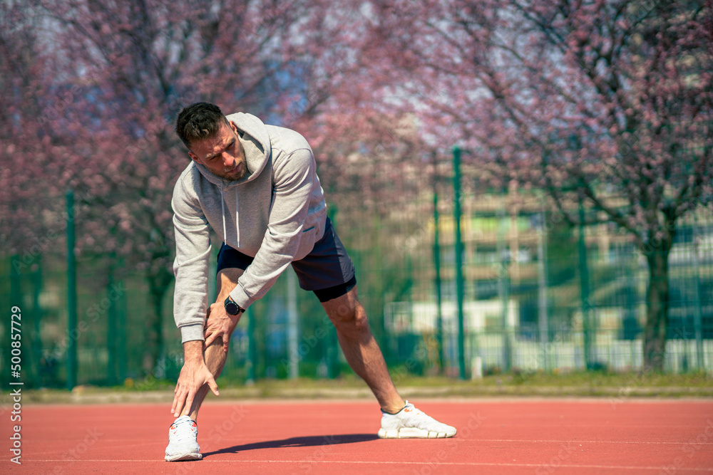 A muscular athlete stretches before a sports training session at a sports stadium A muscular athlete stretches before a sports training session at a sports stadium