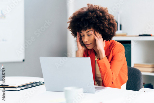 Businesswoman with head in hands sitting with laptop at desk in office photo