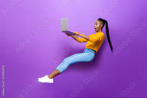 Astonished black woman levitating while working on laptop