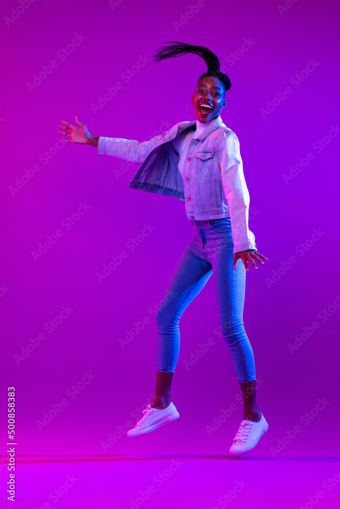 Full body portrait of ecstatic African-American woman jumping in modern neon light studio background Full body portrait of ecstatic African-American woman jumping in modern neon light studio background