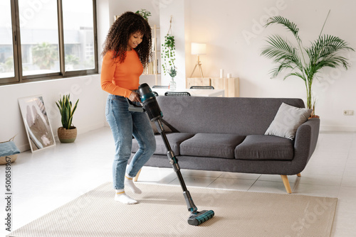 Young woman with vacuum cleaner doing housework at home photo