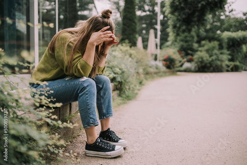 Stressed woman with head in hands sitting on wall at park