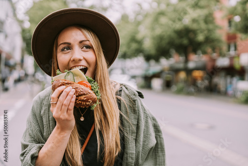 Young woman with hat eating sandwich on street photo