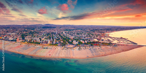 Fototapeta Naklejka Na Ścianę i Meble -  Panoramic summer view from flying drone of Libera Rimini public beach. Amazing evening scene of Italy, Europe. Stunning sunset on Adriatic coast. Vacation concept background..
