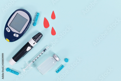 Diabetes treatment equipment with blood glucose sugar meter, lancet, insulin vial and syringe on blue background