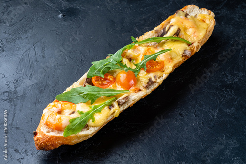 Pizza sandwich. Pizza cooked on a baguette with cheese, tomatoes, shrimps and arugula on a dark table.
