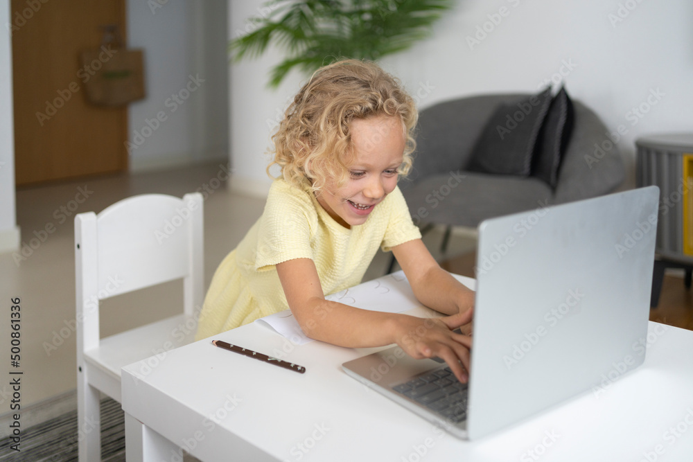 Happy blond girl using laptop sitting at table in living room