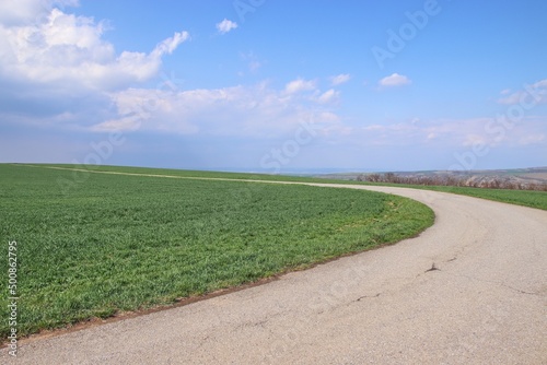 A curve on the road between the green field and blue sky above at Popice, Czech republic