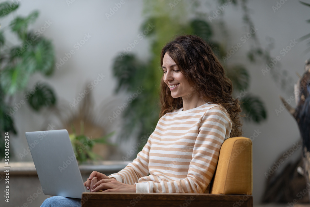 Freelancer woman sitting in armchair in green house, working on laptop surrounded by houseplant. Home garden, remote work, distance job. Female typing text on computer in cozy apartment with plants. Freelancer woman sitting in armchair in green house, working on laptop surrounded by houseplant. Home garden, remote work, distance job. Female typing text on computer in cozy apartment with plants.