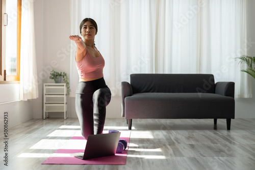 Fototapeta Naklejka Na Ścianę i Meble -  Young asian fitness trainer give yoga video lesson show stretching exercise before laptop webcam in conference mode. Motivated female take part in virtual sport training