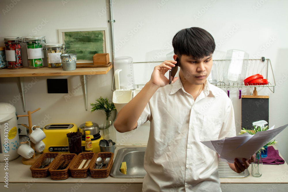 Remote work concept, Male freelancer read business document and talking with client in kitchen room Remote work concept, Male freelancer read business document and talking with client in kitchen room
