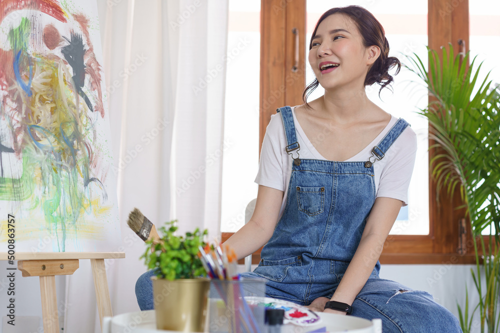 Creative of art concept, Young asian woman hold paint brush and happy to look on art masterpiece