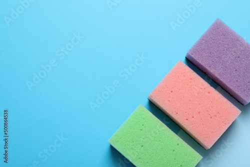New sponges on light blue background, flat lay. Space for text