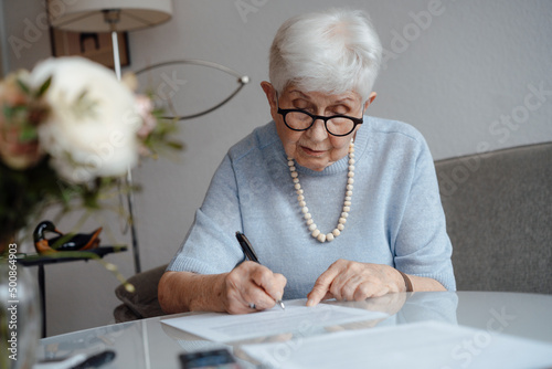 Senior woman writing on paper sitting at home photo
