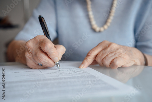 Hands of senior woman writing on paper with pen photo