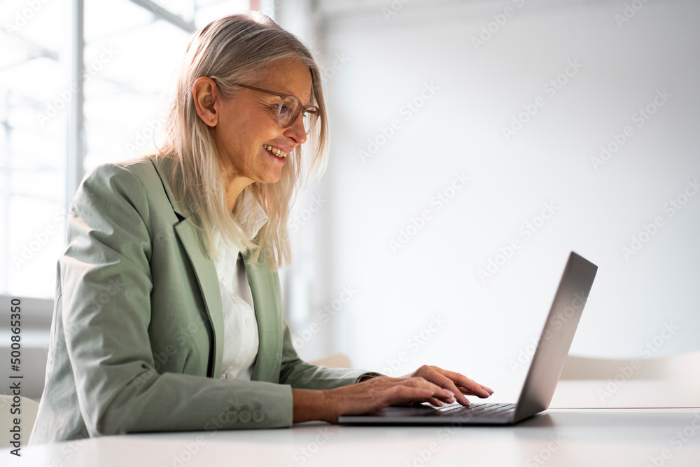 Smiling senior businesswoman working on laptop in office Smiling senior businesswoman working on laptop in office