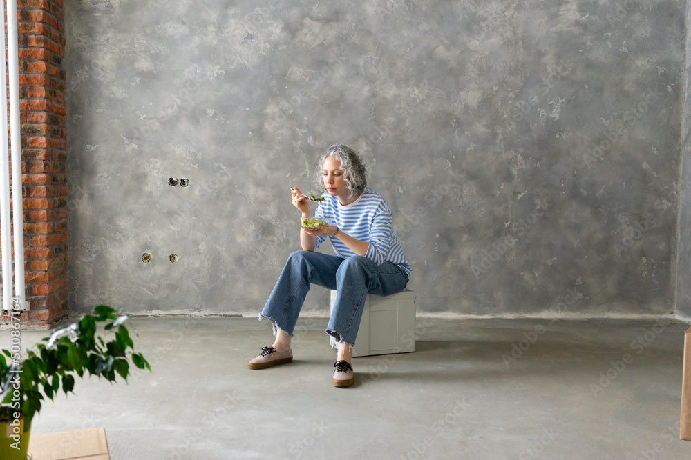Woman eating lunch sitting on box in front of wall