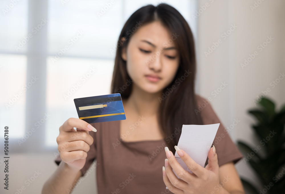 A young Asian woman is stressed because she looks at many expense bills and she has no money to pay them. Not enough money on credit card to pay