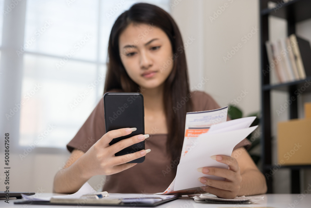 Fototapeta premium A young Asian woman with many expense bills and she using smartphone to calculate and purchase with scan qr code payment online.