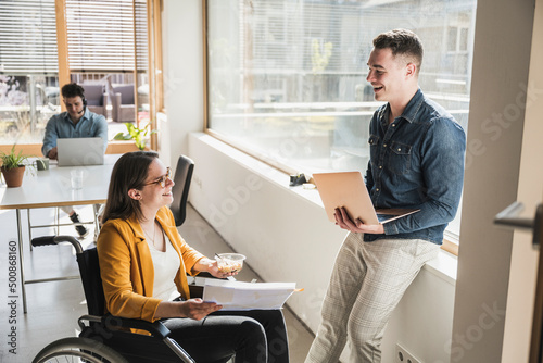 Smiling businessman talking to female colleague in wheelchair in office