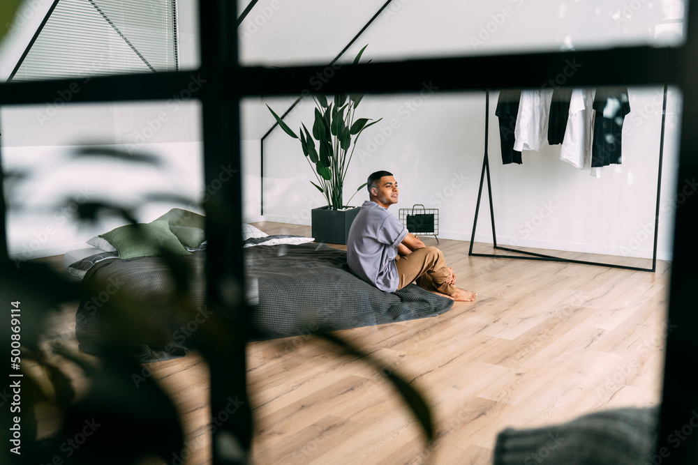 Young man sitting on bed seen through glass at home Young man sitting on bed seen through glass at home