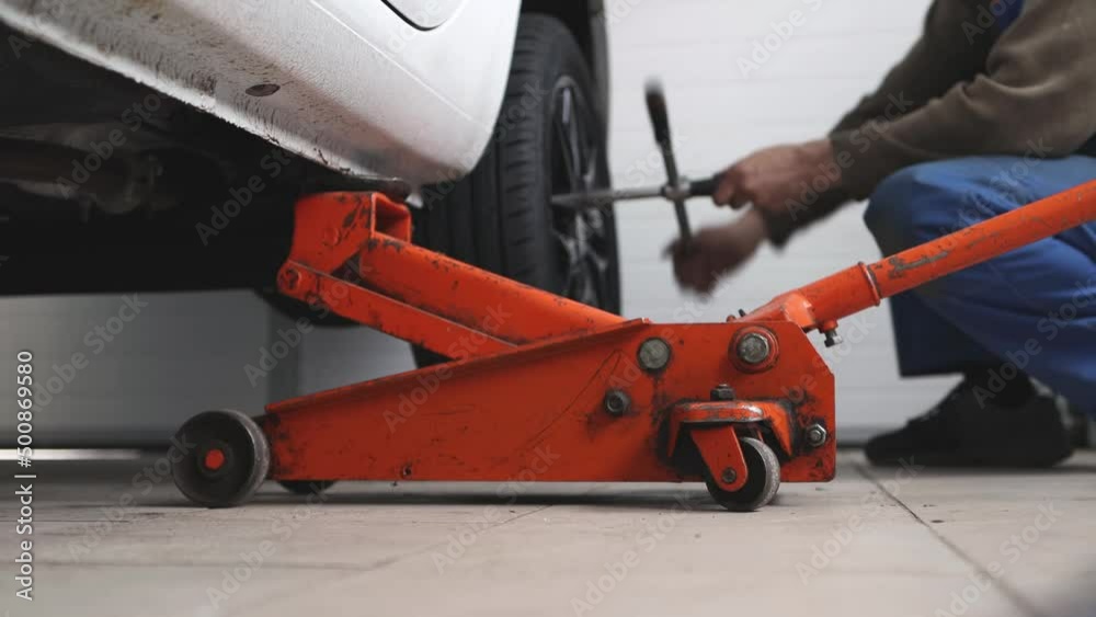 Mechanic unscrews wheel bolts, replacement of worn parts, focus on bright orange car lift. Mechanic unscrews wheel bolts, replacement of worn parts, focus on bright orange car lift.