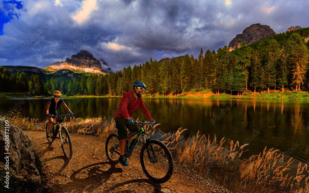 Cycling outdoor adventure in Dolomites. Cycling woman and man on electric mountain bikes in Dolomites landscape. Couple cycling MTB enduro trail track. Outdoor sport activity.