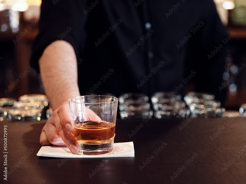Male bartender serves a glass of neat whiskey at the pub
