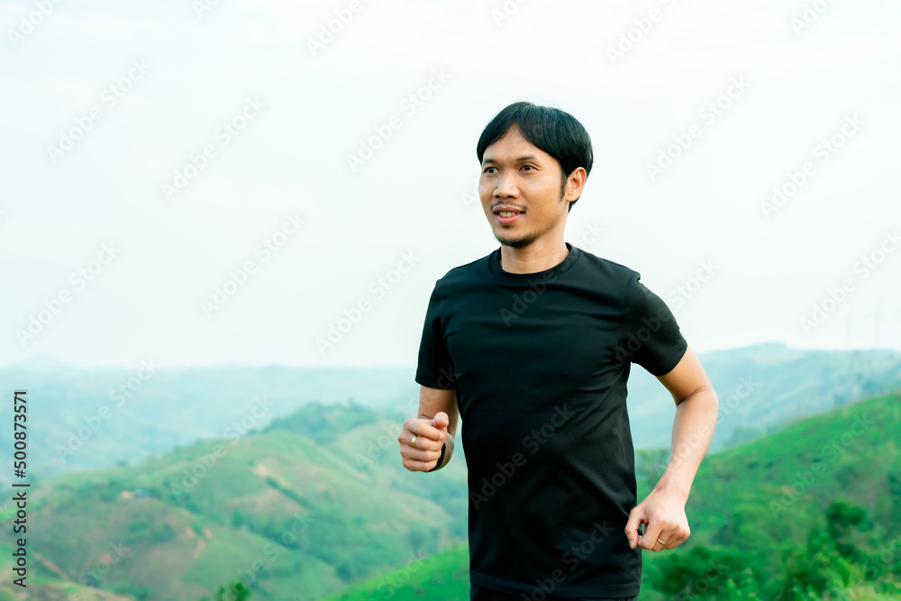 Portrait of half-body portrait of Asian male runner in black training on a high mountain. The back view is high mountain, with beautiful scenery. In the evening the air is fresh and atmosphere is good