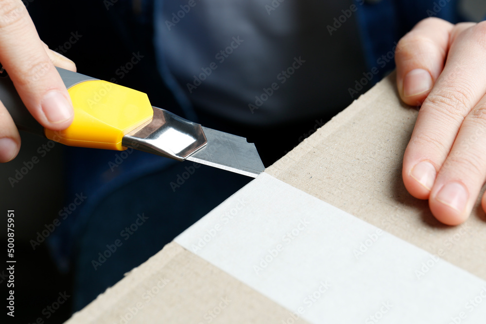 Man using utility knife to open parcel, closeup