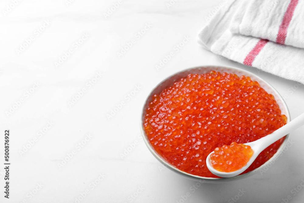 Bowl and spoon with delicious red caviar on white table. Space for text Bowl and spoon with delicious red caviar on white table. Space for text