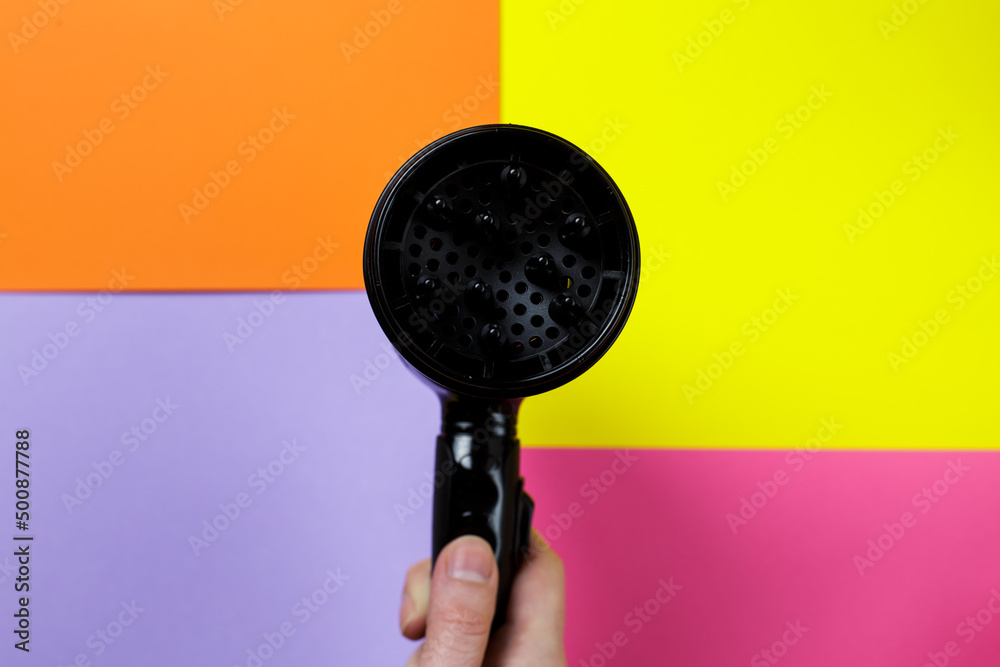 Fashionable bright trendy colors. a woman's hand holds a hair dryer next to a multi-colored background. stylist equipment. Fashionable bright trendy colors. a woman's hand holds a hair dryer next to a multi-colored background. stylist equipment.