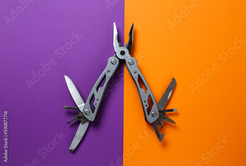 multitool lies on a multi-colored background. multitool with open tools.