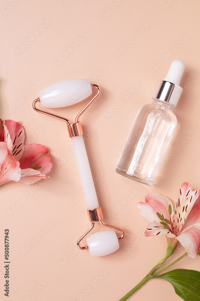 Glass bottle with oil, face roller for face massage on a beige background with flowers. Cosmetic facial skin care and spa. Natural treatment concept. Glass bottle with oil, face roller for face massage on a beige background with flowers. Cosmetic facial skin care and spa. Natural treatment concept.