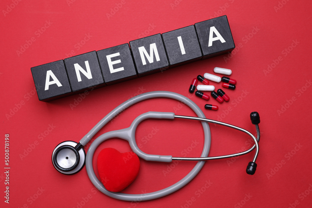 Word Anemia made with black wooden cubes, pills, stethoscope and decorative heart on red background, flat lay Word Anemia made with black wooden cubes, pills, stethoscope and decorative heart on red background, flat lay