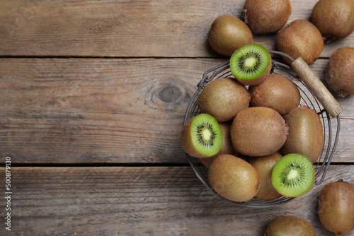 Metal basket with cut and whole fresh kiwis on wooden table, flat lay. Space for text