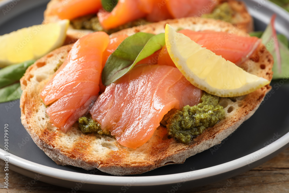Delicious bruschetta with salmon and pesto sauce on wooden table, closeup