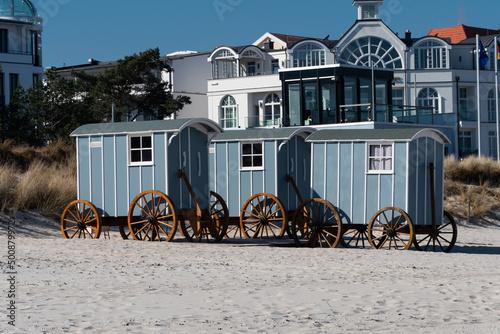Blick vom Strand auf die Promenade von Binz auf Rügen. Auf dem Strand stehen Wagons, Strandwagen, die als Umkleide dienen