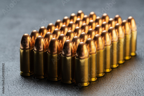Group of aligned 9 mm bullets for handgun isolated on dark background viewed from side. Gun control, crime, military-industrial complex or defense concepts. photo