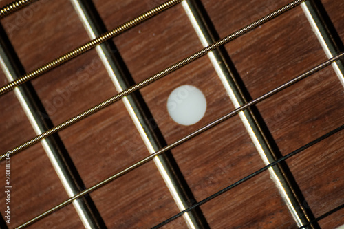 Close-up of steel strings and mahogany wood fretboard with white dot inlay on classical guitar