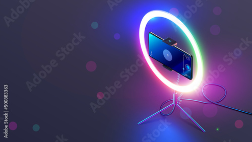 Phone on RGB led ring light on tripod on table. Smartphone streams video in internet. Vlogging concept. Color smart lamp for shoot a video or selfie through camera phone in the dark on desk.