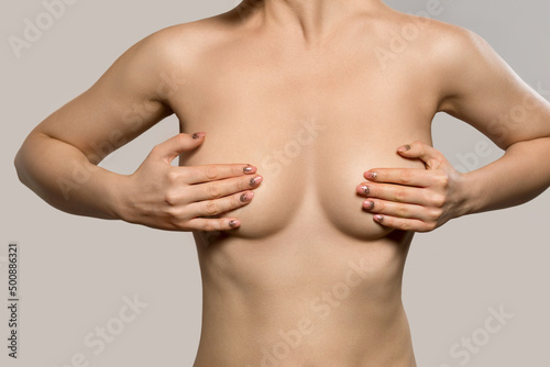 Woman with breast pain touching chest and controlling breast for cancer against a grey background.Female body before pastic surgery. Female healthcare concept.
