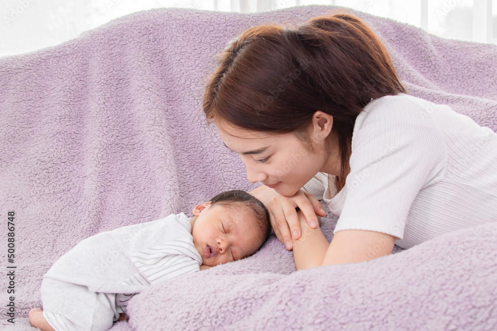Asian mother looking  of babies with love and care. Single mom and newborn baby  is sleeping on bed. Newborn baby aged 0-1 months lying in bed, Cute baby in natural motion. Copy space for text.