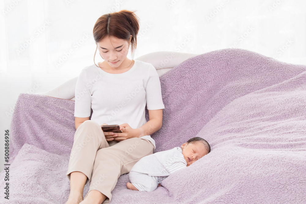 Close up of mom asian playing on her phone while her son is sleeping, Single moms are busy with work. Talking to a friend while the son is sleeping, Mom using the phone. Close up of mom asian playing on her phone while her son is sleeping, Single moms are busy with work. Talking to a friend while the son is sleeping, Mom using the phone.