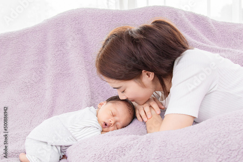 Single mom support and tenderly cuddles the newborn baby gently while the infant is sleeping on bed. Asian mother touching on the back of babies with love and care.