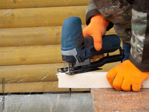 Wallpaper Mural a man saws timber with an electric jigsaw, construction and repair in a country house Torontodigital.ca