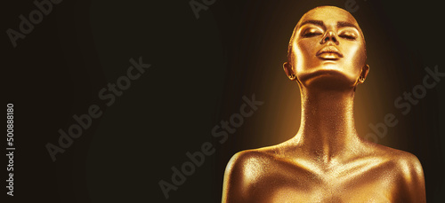 Fashion art golden skin woman face portrait closeup. Model girl with holiday golden Glamour shiny professional makeup. Gold jewellery, jewelry, accessories. Beauty gold metallic body, Lips and Skin