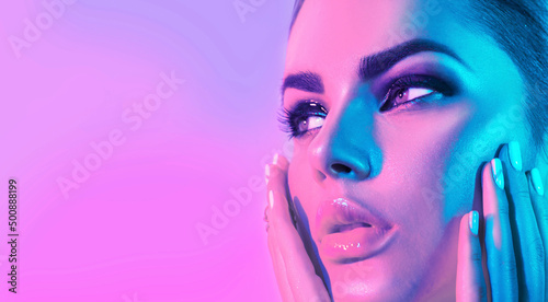 High Fashion model girl face in colorful bright UV lights in studio, portrait of beautiful woman with trendy make-up and manicure. Art design, colorful make up. Over colourful purple, blue background