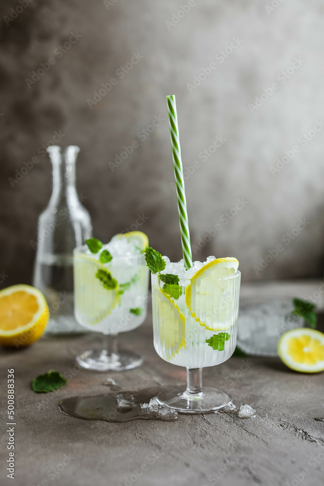 Two beautiful glasses with a cooling citrus drink. Lemonade with lemon, mint and crushed ice.