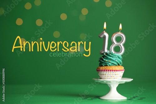 Coming of age party - 18th birthday. Delicious cupcake with number shaped candles on green background. Anniversary celebration